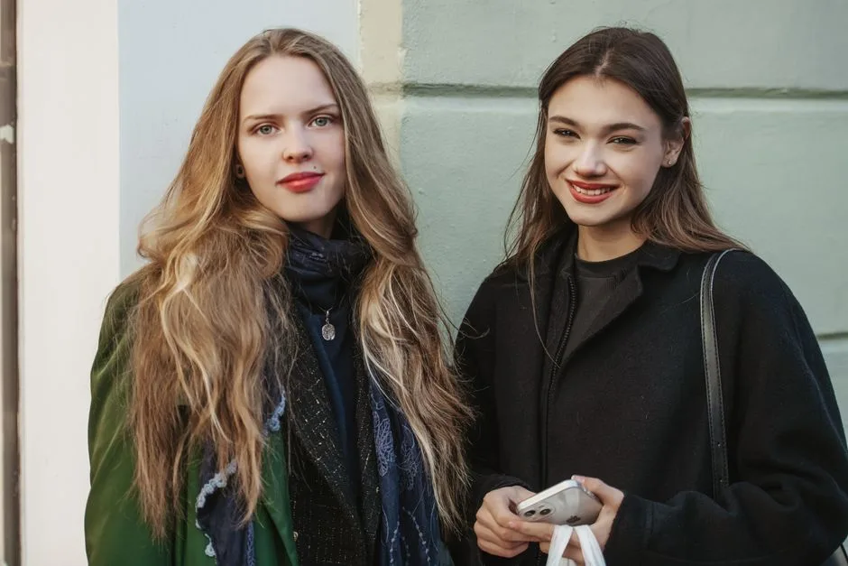 Two young women smiling in stylish coats, capturing autumn fashion and friendship.
