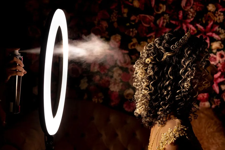Side profile of a woman with curly hair being styled with hairspray under a ring light, perfect for beauty themes.