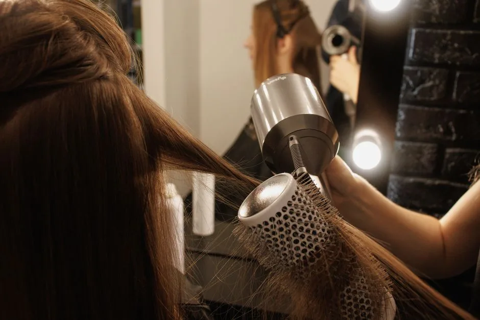 Stylistka suszy włosy kobiety suszarką i szczotką w salonie