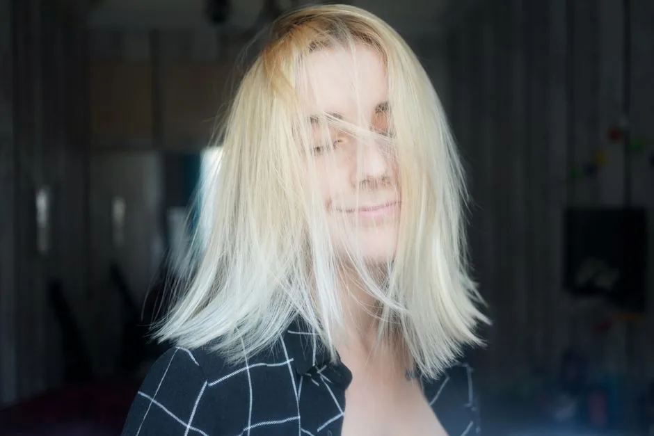 Uśmiechnięta młoda kobieta z potarganymi blond włosami stoi w pokoju z zamkniętymi oczami